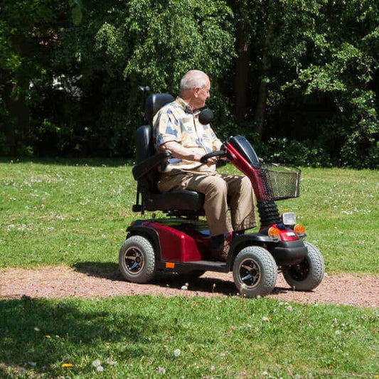 Man using a red mobility scooter on a grassy path in a park.