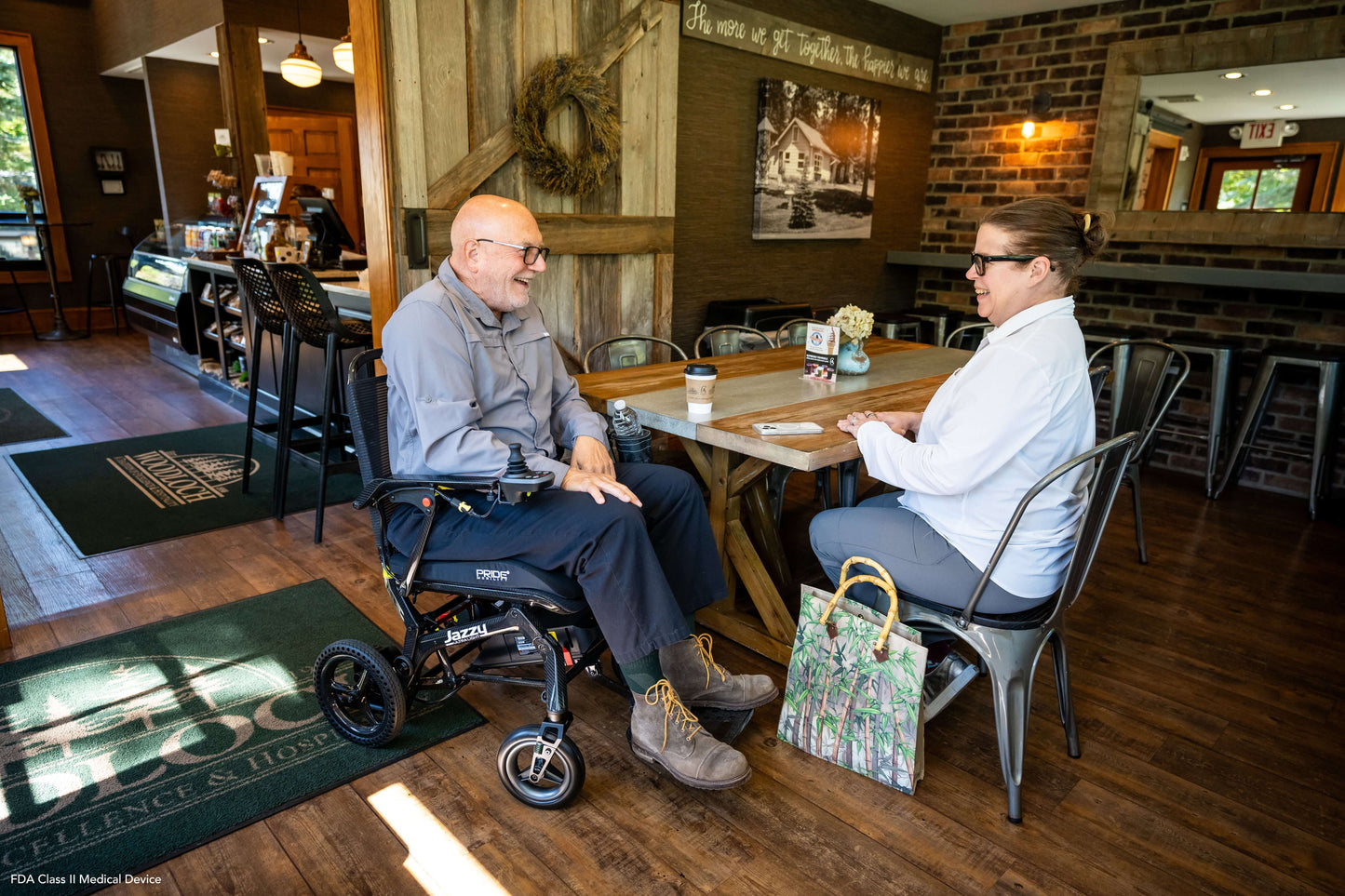 Two people enjoying a conversation in a café, one using a Jazzy Ultra Light power wheelchair.