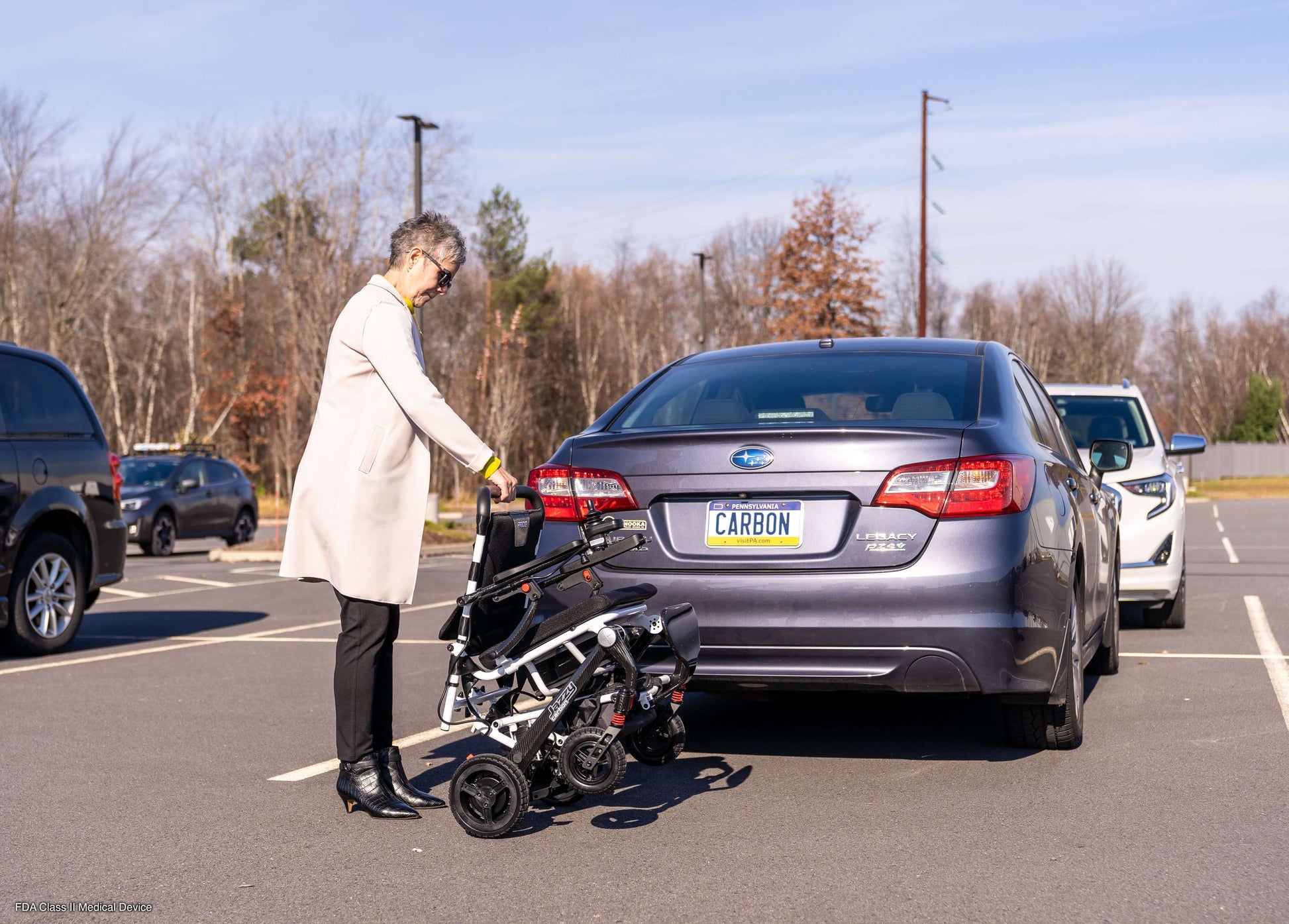 A woman loading a Jazzy® Carbon Power Chair into the trunk of a car in a parking lot, showcasing its portability.