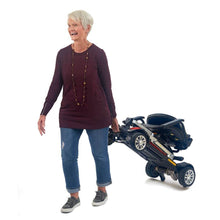Senior woman happily carrying the Buzzaround CarryOn folding scooter, showcasing its portability and ease of use.